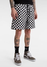 Sort-hvide ternede shorts med elastisk talje og snor. Båret med brune høj-top sneakers og sorte sokker.