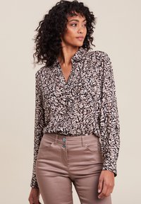 Blusa a maniche lunghe in un tessuto leggero e stampato, caratterizzata da un mix di disegni beige e neri, abbinata a pantaloni beige aderenti.