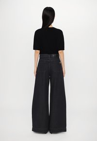 Chemise noire surdimensionnée à manches courtes associée à un jean denim noir à jambes larges, taille haute, avec deux poches arrière.