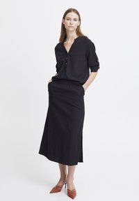 Blusa nera in lino con scollo a V e chiusura a bottoni, abbinata a una gonna nera con vita elastica e scarpe col tacco a punta rosso a strisce.