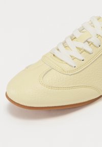 Sneaker gialla in pelle con finitura testurizzata, punta arrotondata, lacci bianchi e suola in gomma. Design minimalista con dettagli di cucitura sottili.