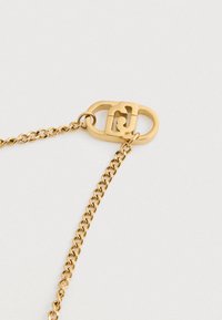 Zlatý náhrdelník s unikátnou oválnou sponou, ktorá obsahuje prepojené otáčajúce sa časti na bielom pozadí.