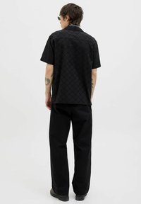 Schwarzes Kurzarmhemd mit einem Rautenmuster, ausgestattet mit einer glatten Textur und einem kragenlosen Halsauschnitt, kombiniert mit lockeren schwarzen Hosen.