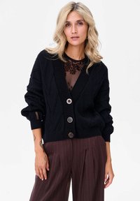 Czarny sweter z dzianiny z dekoltem w serek, wzorem w romby i dwoma dużymi guzikami. Posiada teksturowane rękawy i luźny krój.