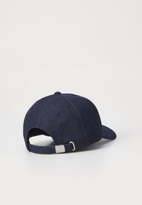 Dunkelblaue Denim-Baseballmütze mit gebogenem Schirm, verstellbarem Metallverschluss und verstärkten Nähten. Strukturiertes Gewebe sichtbar.