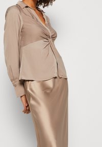 Satinblus i beige med draperad design och krage, tillsammans med en slät, matchande satinkjol. Knapprade manschetter på ärmarna.