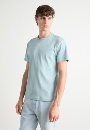 Light blue cotton t-shirt with a round neckline and short sleeves. Features a small white logo on the chest and a smooth, soft texture.