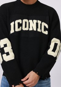 Black knitted sweater featuring "ICONIC" in white on the front, with white numbers "0" and "3" on the sleeves and distressed hem details.