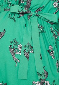 Grön klänning i mjukt tyg med svart leopard- och blomtryck, åtdragen i midjan med en knytbälte.