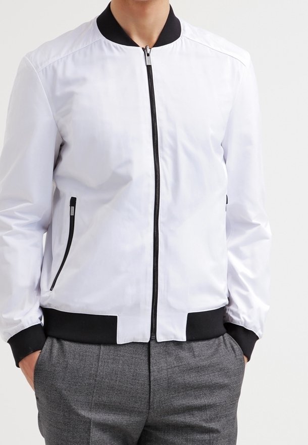 Veste bombers blanche avec col et ourlet côtelés noirs, dotée de poches latérales zippées et d'un tissu lisse et léger.