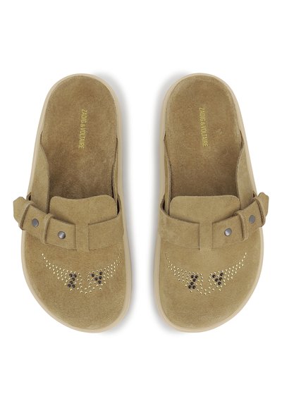 Μπεζ σουέντ παπούτσια που φοριούνται χωρίς κορδόνια, με στρογγυλεμένο σχήμα, διακοσμητικά καρφιά και φαρδιά λωρίδα με δύο μαύρα κουμπιά.