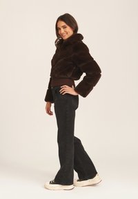 Brown faux fur cropped jacket with a high collar and wide sleeves, worn over dark flared jeans and white-soled sneakers.