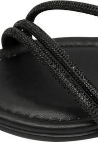Chancla negra con tiras de goma texturizadas que presentan un patrón de tachuelas, reposando sobre una base negra suave con bordes curvados.