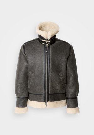 Tummanharmaa nahkatakki, jossa on tekoturkiskaulus, vetoketjusuljenta ja mustat yksityiskohdat hihansuissa ja helmassa. Takissa on pystysuorat saumat ja rento istuvuus.