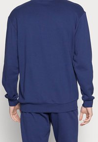 Granatowa bluza z okrągłym dekoltem o luźnym kroju, z prążkowanymi mankietami i ściągaczem u dołu. Wykonana z teksturowanego materiału o gładkim, jednolitym kolorze.