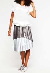 Bílý ruffled top doplněný kovovým plisovaným sukní po kolena, přecházející z tmavě šedé do stříbrné. Stříbrné tenisky dotvářejí vzhled.