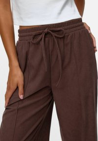 Pantalons jogger marron à côtes, avec une taille élastique et un cordon de serrage. Dotés de poches latérales et d'une coupe décontractée pour le confort.