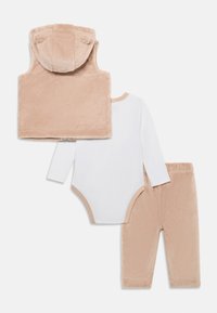 Troslojni baby outfit: bež plišasta bezrukavna prsluk s kapuljačom, bijeli bodi s dugim rukavima i usklađene bež meke hlače.