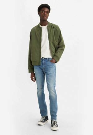 Oliven grøn bomberjakke, hvid t-shirt, lyseblå jeans og sorte højtop sneakers. Casual fit, glat tekstur og klassisk design.