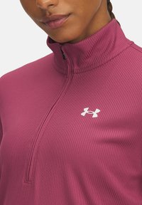 Tæt siddende, ribbet zip-up top i mørk pink med høj krave. Har en hvid logo på den øverste venstre side og en glat tekstur.