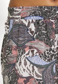 Tissu à motifs floraux avec de grandes feuilles dans des tons de vert, bleu et marron sur un fond rose ; détail de taille élastique visible.