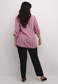 Rosa randig blus med rullade 3/4 ärmar, tillsammans med svarta byxor och klackar. Blusen har vertikala tunna ränder för kontrast.