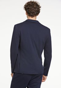 Blazer azul marino de tela texturizada, con una abertura trasera, solapas de muesca y puños abotonados. Corte entallado y líneas limpias.