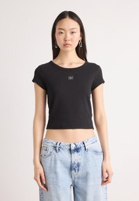 Black cropped t-shirt made of cotton with a round neckline and short sleeves, featuring a small logo on the front. Paired with light blue jeans.