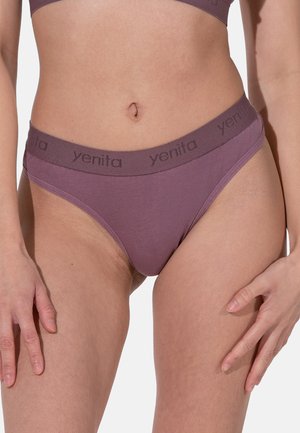 Femme portant un ensemble de sous-vêtements mauve avec une ceinture élastique de marque "yenita" visible, cadrée au niveau du torse et des cuisses, sur un fond uni.