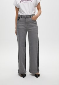 Grijze wijde jeans met zwarte zijpanelen, met voordo pockets, een knoopsluiting en een rechte pasvorm. Glad denimtextuur.