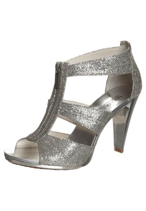 Srebrne sandały na wysokim obcasie wykonane z błyszczącego materiału, z ażurowym wzorem, regulowanym zamkiem i błyszczącym metalicznym obcasem.