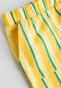 Geel gestreepte stof met turquoise verticale lijnen, voorzien van een elastische tailleband en een zachte textuur. Vouwen zichtbaar aan de bovenkant.