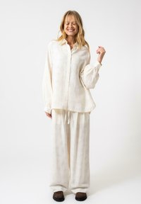 Camicia button-up a maniche lunghe di colore crema chiaro con un motivo testurizzato e maniche a sbuffo, abbinata a pantaloni a gamba larga coordinati.