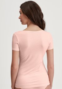 Light pink short-sleeve shirt with a rounded neckline, fitted design, and smooth texture, showing the back view and contours of the body.