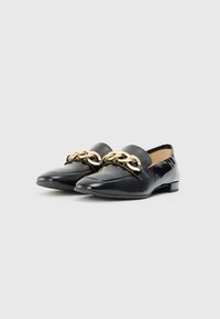 Black patent leather loafers with a low heel, featuring a gold chain accent across the upper and a smooth texture.