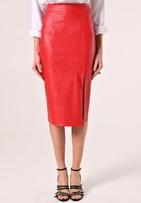 Roter Kunstleder-Bleistiftrock mit hoher Taille, vorderem Schlitz und glatter Textur, kombiniert mit schwarzen Riemchensandalen.