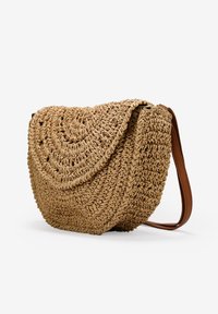 Bolso de paja tejido tipo bandolera con forma redondeada, color natural beige y una correa de cuero marrón, que presenta un diseño espiral texturizado.
