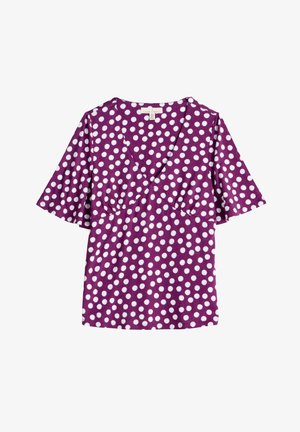 Lilla kortærmet top med V-hals, der har hvide prikkede mønstre, en samlede bustedetalje og løse flæseærmer.