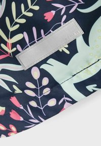 Mörkt tyg med färgglad blommönstring och en sydd rektangulär reflexnamnsskylt fäst i mitten.