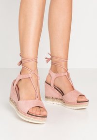 Růžové semišové wedges sandály s otevřenými prsty, křížovými řemínky kolem kotníků a spletenými jutovými detaily na podrážce, s hladkým povrchem a zaoblenými okraji.