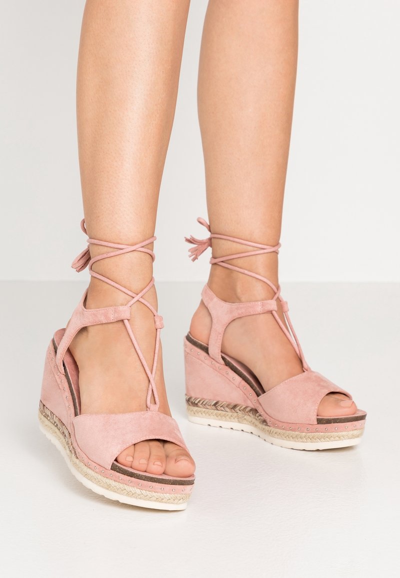 Růžové semišové wedges sandály s otevřenými prsty, křížovými řemínky kolem kotníků a spletenými jutovými detaily na podrážce, s hladkým povrchem a zaoblenými okraji.