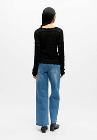 Schwarzer strukturierter Langarmpullover mit gemustertem Detail, kombiniert mit hochtaillierten hellblauen weiten Jeans und schwarzen Blockabsatzstiefeln.