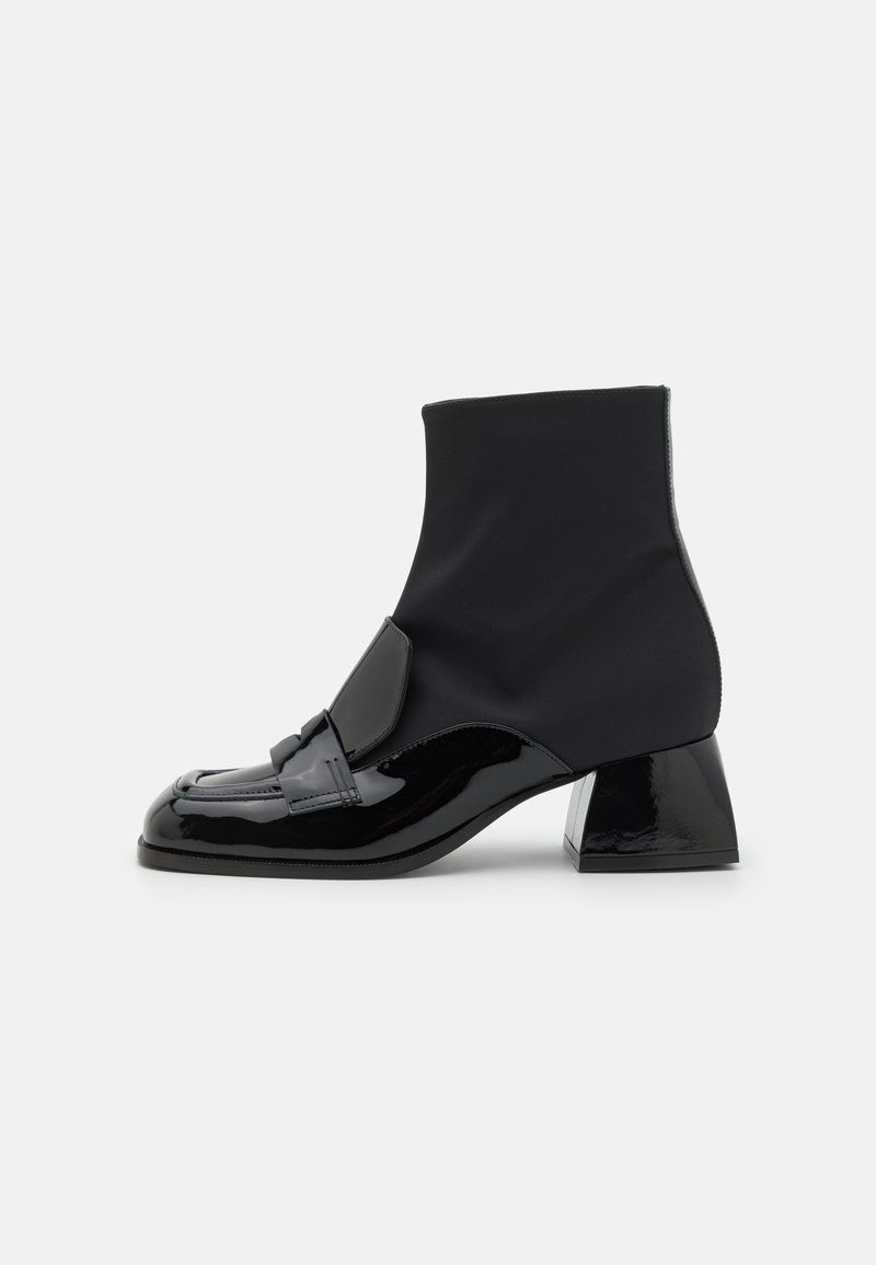 Bottines noires avec un bout en cuir verni brillant et un upper en tissu extensible structuré, dotées d'un talon carré bloc et de quincaillerie décorative.