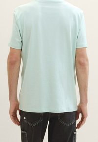 Tyrkysové krátkosrsté tričko vyrobené z jemné látky, s rovním střihem a kulatým výstřihem, nošené s tmavými džínami.