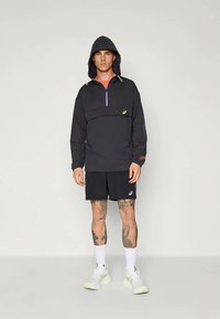 Černá mikina s kapucí a polo zipem na přední straně, s fialovými a žlutými akcenty. V kombinaci s černými šortkami a bílými sportovními botami.