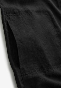 Gros plan sur un tissu noir avec une fente latérale et un détail de couture visible sur un matériau léger et texturé.
