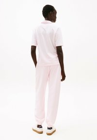 Lys rosa polo-shirt og matchende sweatpants, lavet af blødt stof; har korte ærmer, afslappet pasform og hvide sneakers med brune såler.