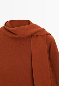 Rostfarbener gestrickter Pullover mit einem breiten, umgeschlagenen Rollkragen und einem angebrachten Schal, der über eine Schulter drapiert ist.