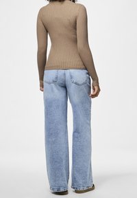 Pull marron côtelé à manches longues associé à un jean bleu clair à jambes larges, muni de poches arrière et d'une finition délavée.