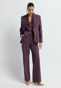 Tailored purple suit with a double-breasted blazer, notch lapels, and golden buttons; paired with wide-leg trousers and nude heels.